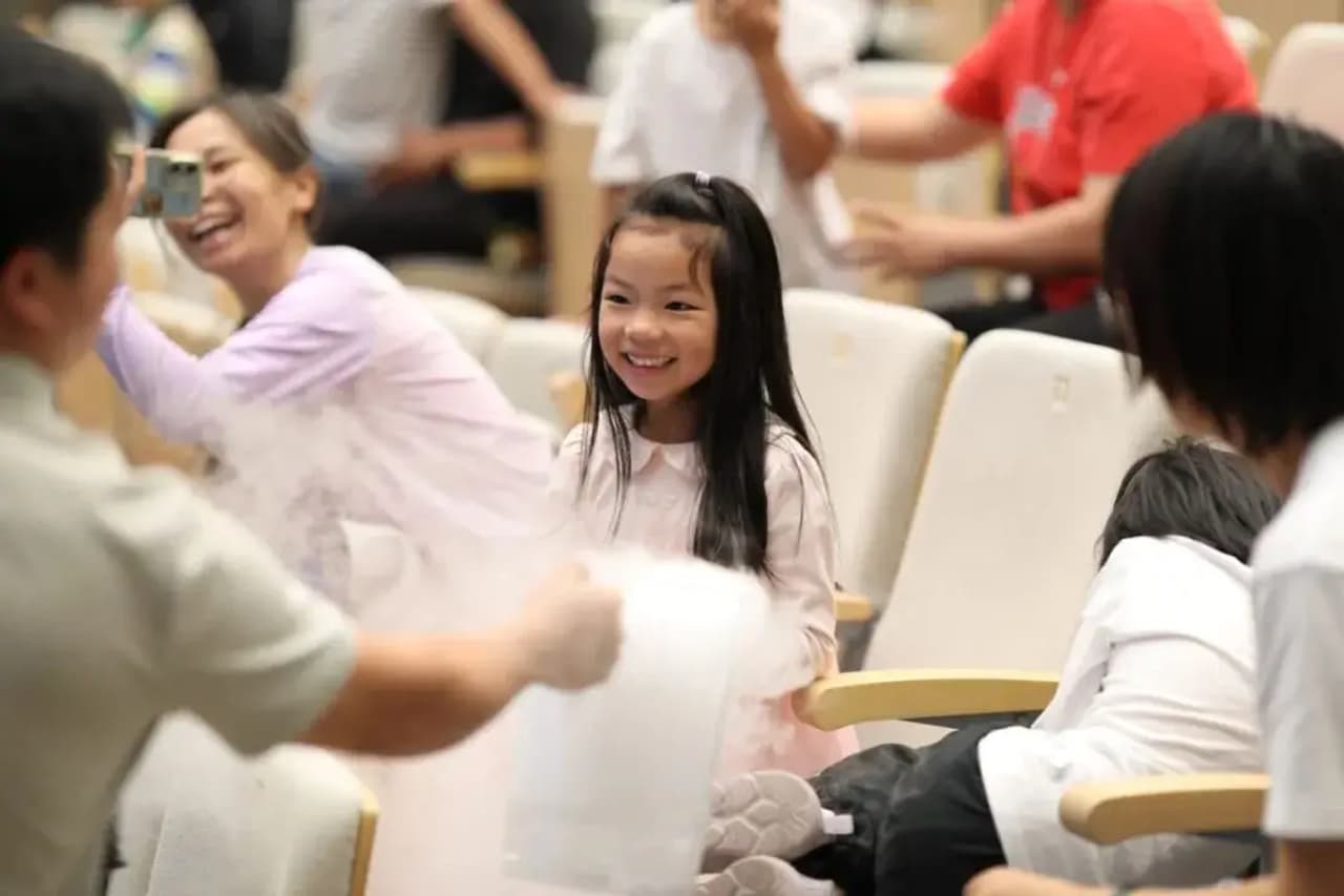 Un grupo de personas en un evento, con una niña sonriendo mientras se realiza una actividad científica.